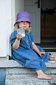 Mädchen sitzt mit einem Glas Milch im Hauseingang