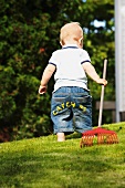 Kleiner Junge mit einem Rechen im Garten