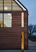 Wohnhaus mit Holzfassade und beleuchteten Fenstern in Dämmerlichtstimmung