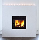 White, projecting masonry fireplace with tea light holders on mantelpiece and burning fire