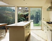 Eine helle Küche mit Kücheninsel und Glasfront zu der Terrasse