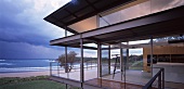 Zeitgenössisches Haus aus Stahl und Glas an Meeresküste mit dramatischer Wolkenstimmung