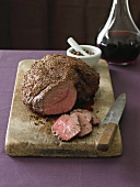 Leg of Lamb on a Cutting Board; Partially Sliced; Decanter of Wine