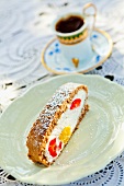 A slice of wholemeal sponge cake, filled with quark cream, mango and strawberries with a cup of mocha in the background