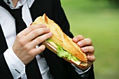 Young man eating baguette sandwich