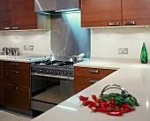 Modern fitted kitchen with broad, stainless steel handles on wooden doors and stainless steel cooker unit