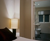 Lit bedside lamp and taupe walls in modern bedroom with ensuite bathroom