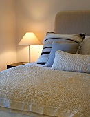 Scatter cushions and bedspread on double bed next to lit bedside lamp