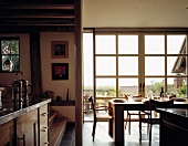 Moderne Wohnküche mit Landhauselementen vor breiter Fensterfront und Blick in die freie Landschaft