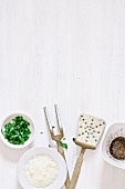 Kitchen utensils and small bowls with parmesan, herbs and spices