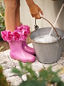 Woman with flowery Wellington boots filling a bucket with water