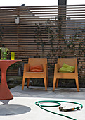 Modern garden chairs and a table in front of a wooden fence on a terrace with a concrete floor