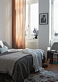 Bett mit verschiedenen Tagesdecken neben Fenster mit Vorhang