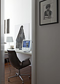 View of retro desk chair at desk with computer through open door