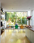 Colourful, Bauhaus shell chairs at dining table in front of floor-to-ceiling glass wall with view of garden