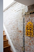 Gelb lackiertes Hängeschränkchen an Treppenhauswand aus Ziegel