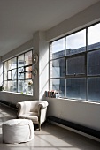 Baroque armchair and modern stool below industrial window in loft apartment