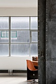 Blick durch offenstehende Schiebetür in Raum auf orangen Schalenstuhl vor Industriefenster