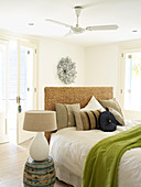 Table lamp on barrel-shaped cabinet next to bed with headboard and various scatter cushions in modern bedroom