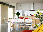 Dining table made of light wood with white plastic chairs in an open kitchen
