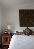 Schlichtes Schlafzimmer mit asiatischem Wandbehang über Bett und antikes Nachtkästchen aus Holz
