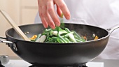 Mixing spring onions with other vegetables in a wok