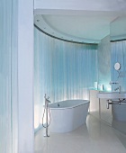 Freistehende Badewanne mit Standarmatur vor gebogener Wand mit Lichtreflexionen