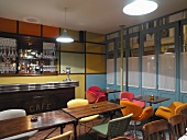 Shell chairs with colourful upholstery and multi-coloured wall panels in retro-style bar