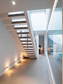 Bottom view of staircase lit by wall spotlights next to glass wall leading to indoor swimming pool