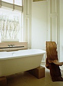 Free-standing modern bathtub supported on wooden blocks and organic, gnarled wood chair