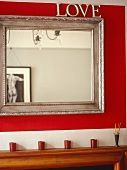 'Love' mirror with silver wooden frame on red wall with reflection of male nude