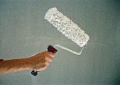 Hand holding a paint roller with white paint