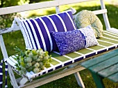 White lacquered garden bench with colorful pillows and seat cushion