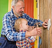 Grandfather and grandson hammering a nail into a wall