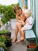 Mother and son on a wooden bench with flower pots on a balcony