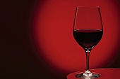 A glass of red wine in front of a red background