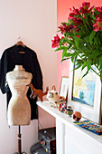 Tailor's dummy and dress hanging up in corner next to bouquet on shelf