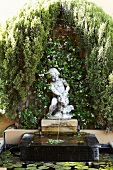 Ornamental fountain with stone figure in front of facade covered with climbers