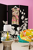 Tea service on side table next to armchair with multi-coloured upholstery in front of black and white screen