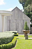 Manicured garden with cyprus trees in antique planters in front of old barn