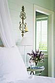 Ländlicher Schlafraum mit Blumenstrauss auf Nachttisch und Blick durch offene Tür auf Fenster