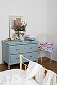 Nostalgic bedroom with pale blue vintage chest of drawers, ornate garden chair and metal bed in foreground