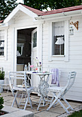 White garden chairs and table in front of summer house with white-painted wooden facade