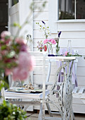 Vase of garden flowers on terrace table in front of white summer house