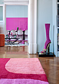 Teppichausschnitt in Pink/Fliedertönen und Schuh-Kunstobjekt; im Hintergrund Essplatz mit weissen Panton-Chairs vor pinkfarbenem Kunstwerk