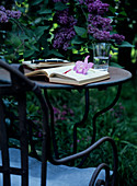 Open book on metal garden table in front of purple flowering lilac