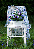 Floral blouse and blue and purple violas on old wooden chair amongst grass