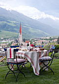 Gedeckter Tisch im Garten mit Blick auf die Ortschaft Schlander mit Kirchturm und auf die Bergkette
