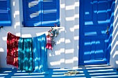 Light and shadow play on a facade of a Mediterranean home with blue window shutters and clothes hanging to dry underneath