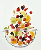 Various fruits falling into glass bowl